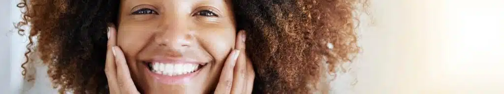 Smiling person with curly hair holding face