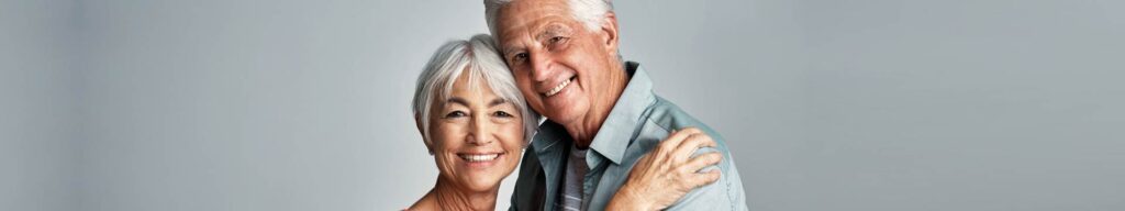 Smiling senior couple embracing against pale background