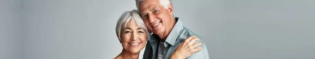 Smiling senior couple embracing against pale background