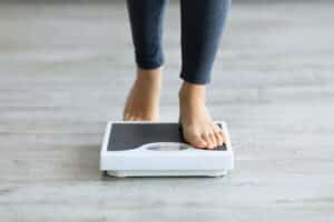Woman stepping on the scale after weight loss with health coaching in Dallas, TX
