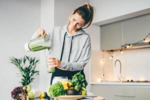 Young woman pouring green smoothie in kitchen
